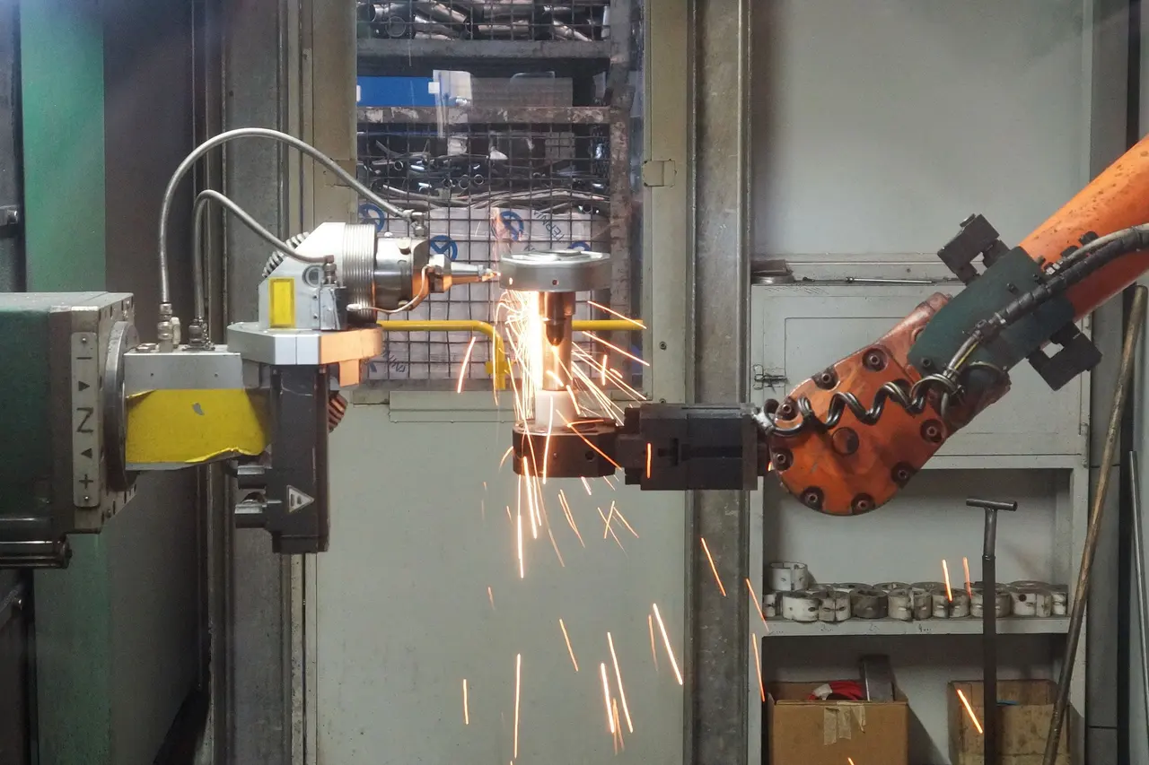 Robot kol kıvılcımlar saçarak çelik parçayı kaynatıyor